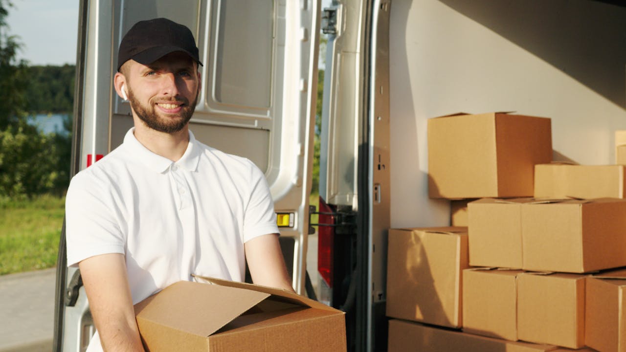 Courier managing deliveries with a panel van, holding boxes outside.